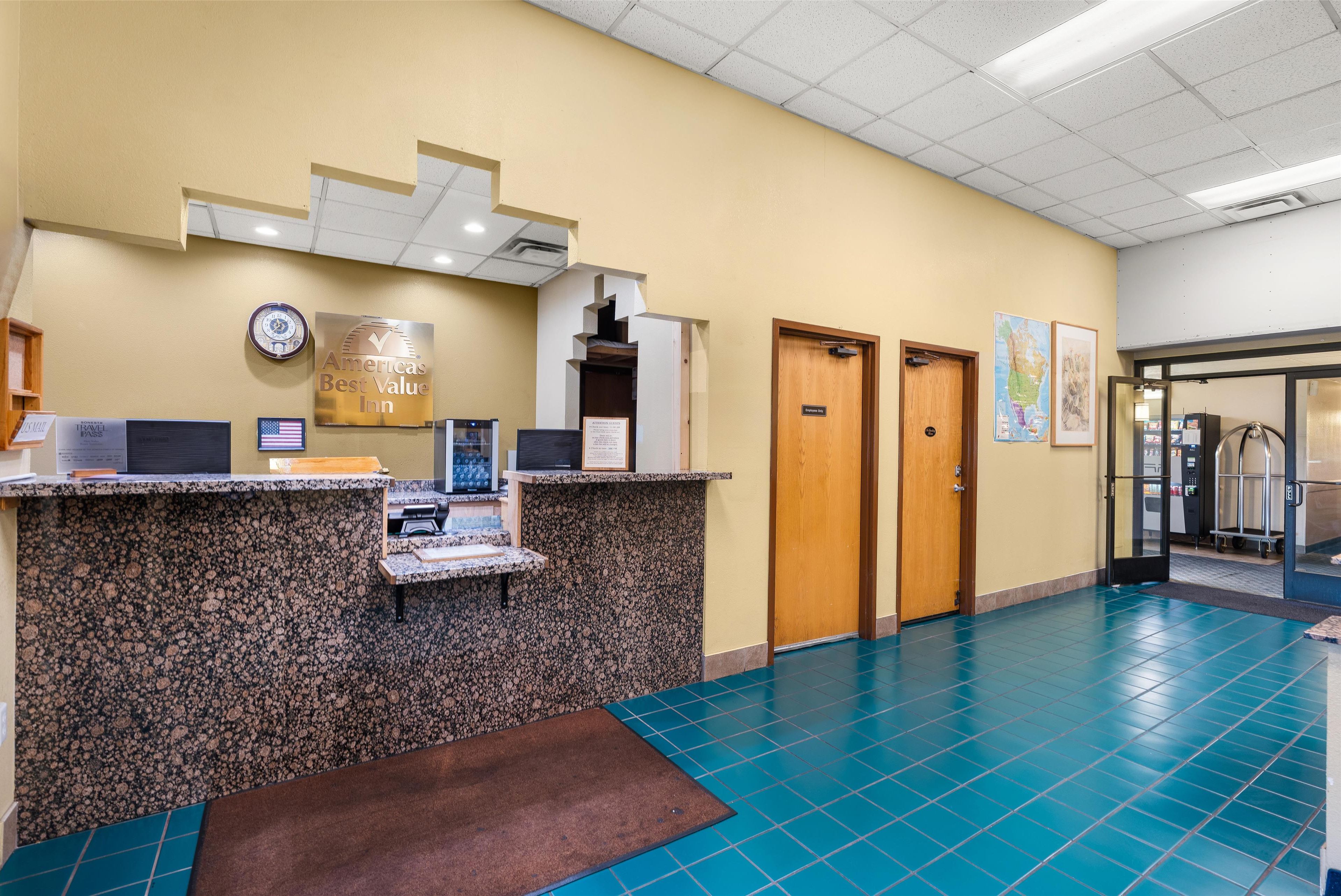 Un mostrador de recepción con un reloj, un letrero que dice 'America's Best Value Inn' y un piso de baldosas azules.