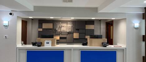 Un comptoir d’accueil d’hôtel au design moderne, comprenant un écran numérique, une enseigne pour Holiday Inn Express & Suites et une caméra de surveillance.