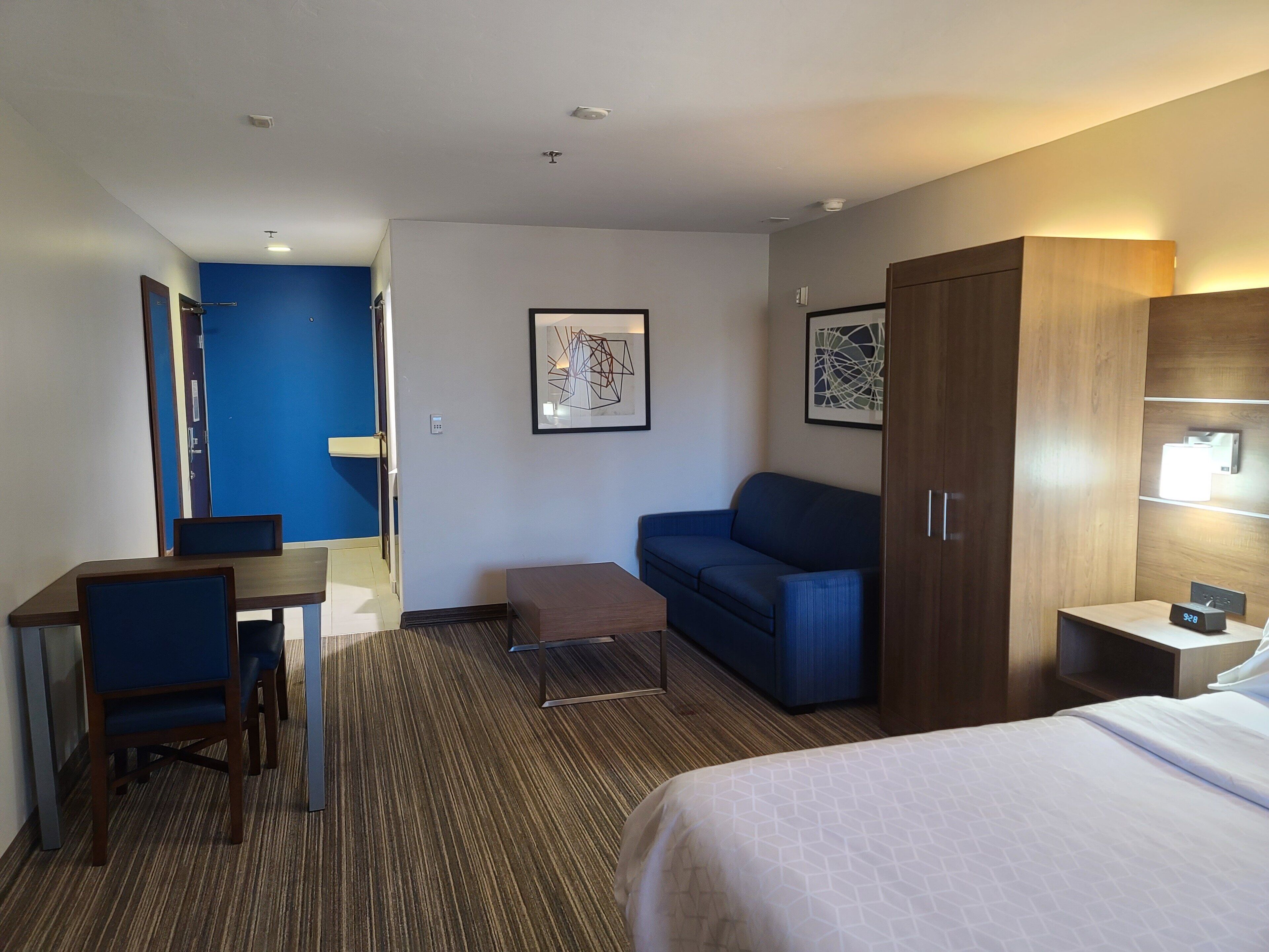 Una habitación de hotel con una cama, un escritorio, una silla, un sofá y un armario.