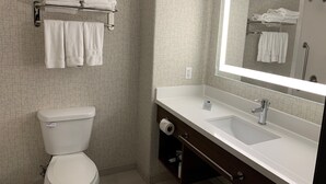 A modern bathroom with a toilet, a sink with a large mirror, and a towel rack with folded towels. - Holiday Inn Express & Suites Woodland Hills by IHG (Woodland Hills)