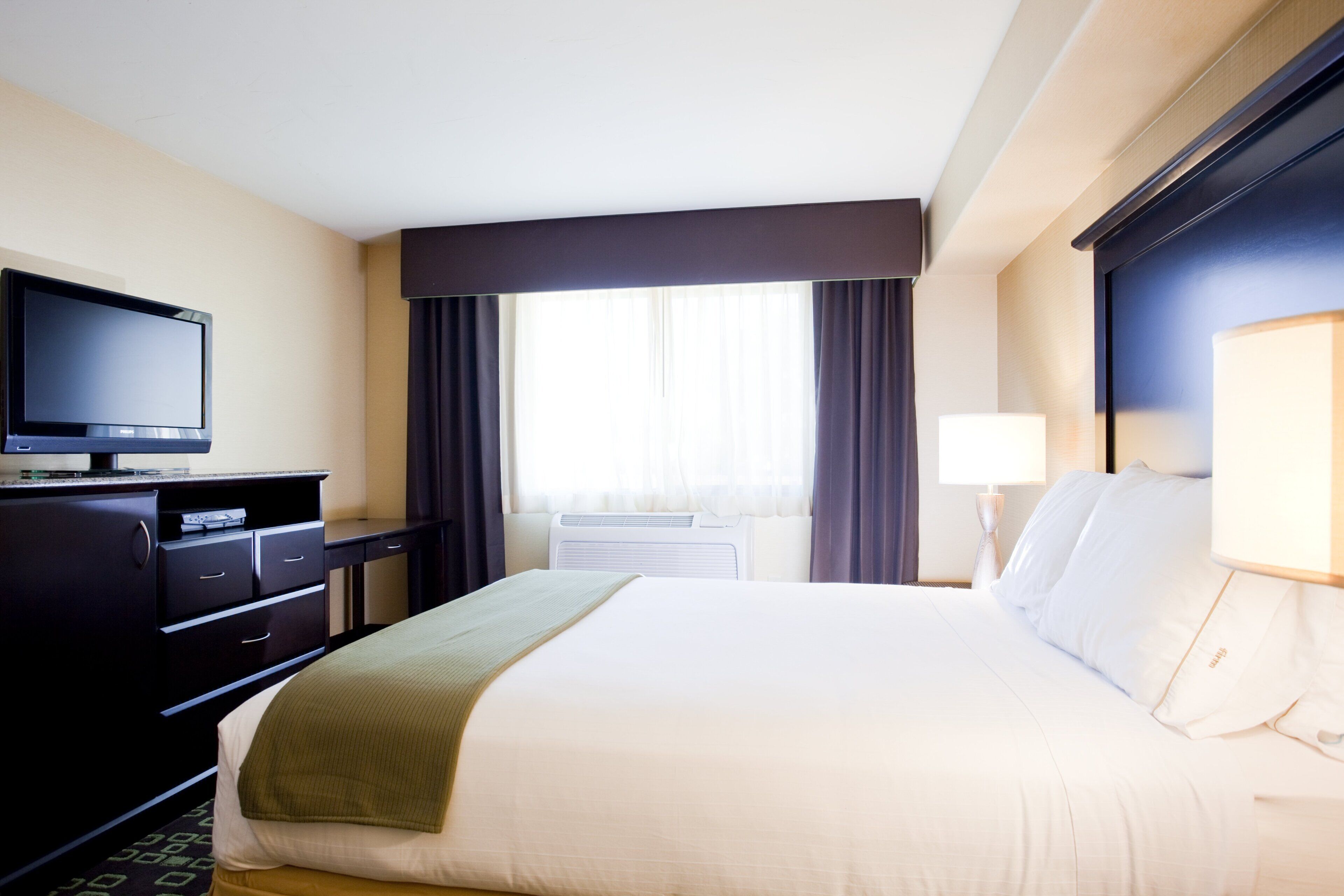 A hotel room with a bed, a television, a desk, and a window with curtains.