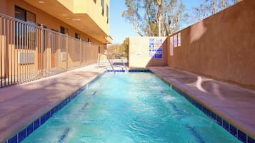 Una piscina con borde de azulejos, cerca metálica y un edificio de fachada plana al fondo.