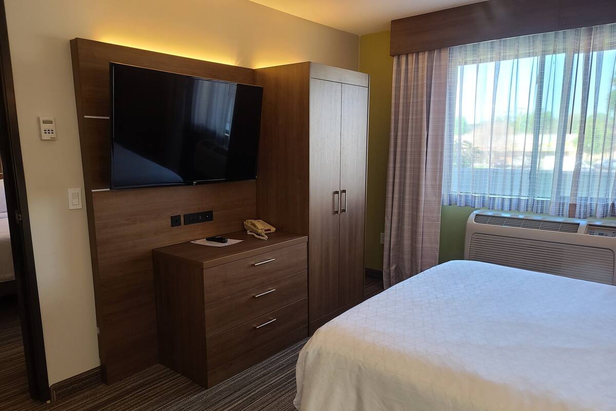 Ein Hotelzimmer mit einem großen Bett, einem flachbildfernseher an einer Holzeinrichtung, einem Telefon und einem Kleiderschrank.