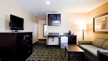 A hotel room with a television, kitchenette, and seating area.