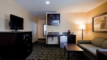A hotel room with a kitchenette, a television, a sofa, a lamp, and a patterned carpet.