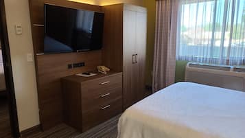 A hotel room with a bed, a TV, a wardrobe, a desk with a phone, and a window with curtains.
