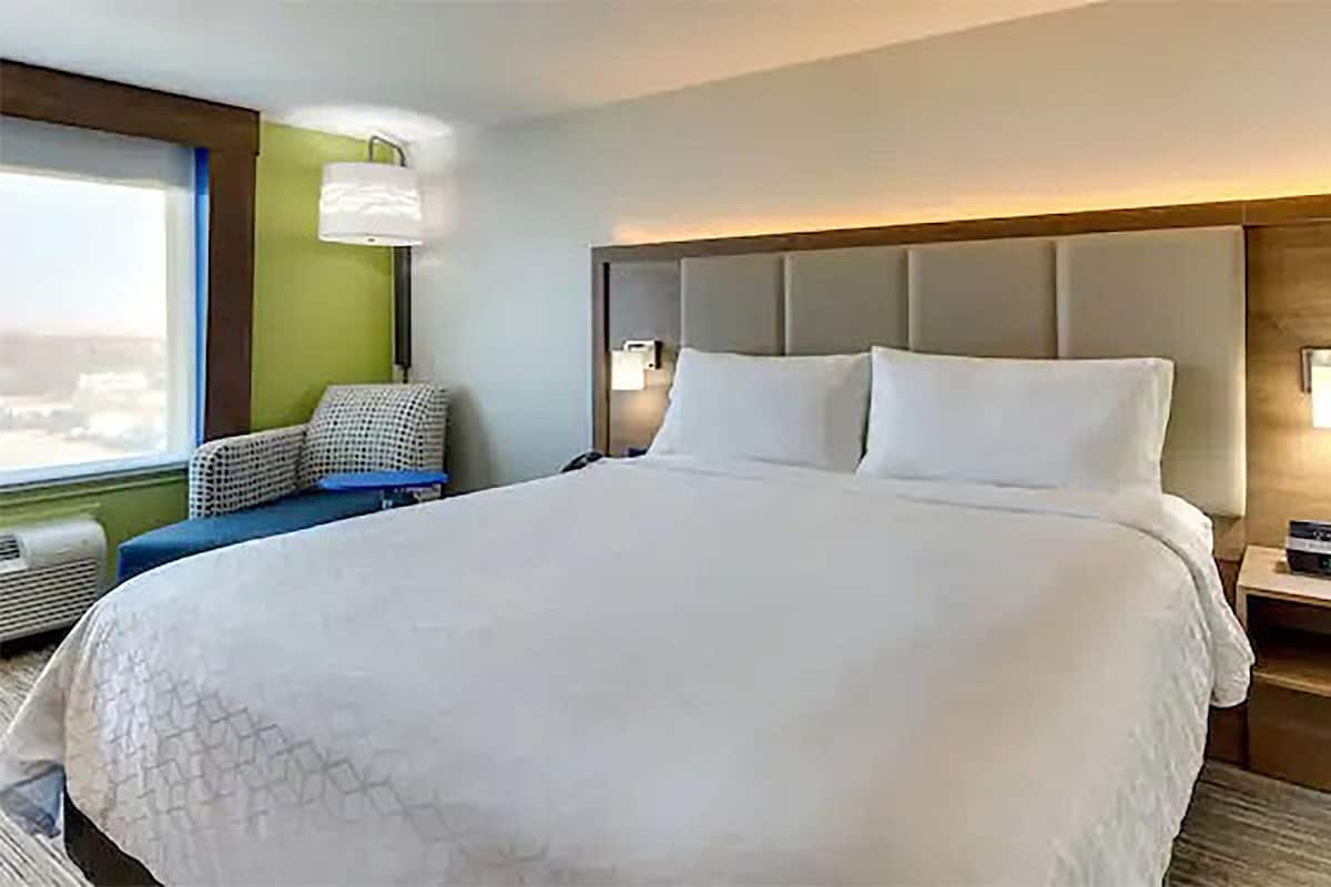 Ein großes Bett mit gepolstertem Kopfteil, ein Nachttisch mit Radio und ein Sessel mit gemustertem Kissen.