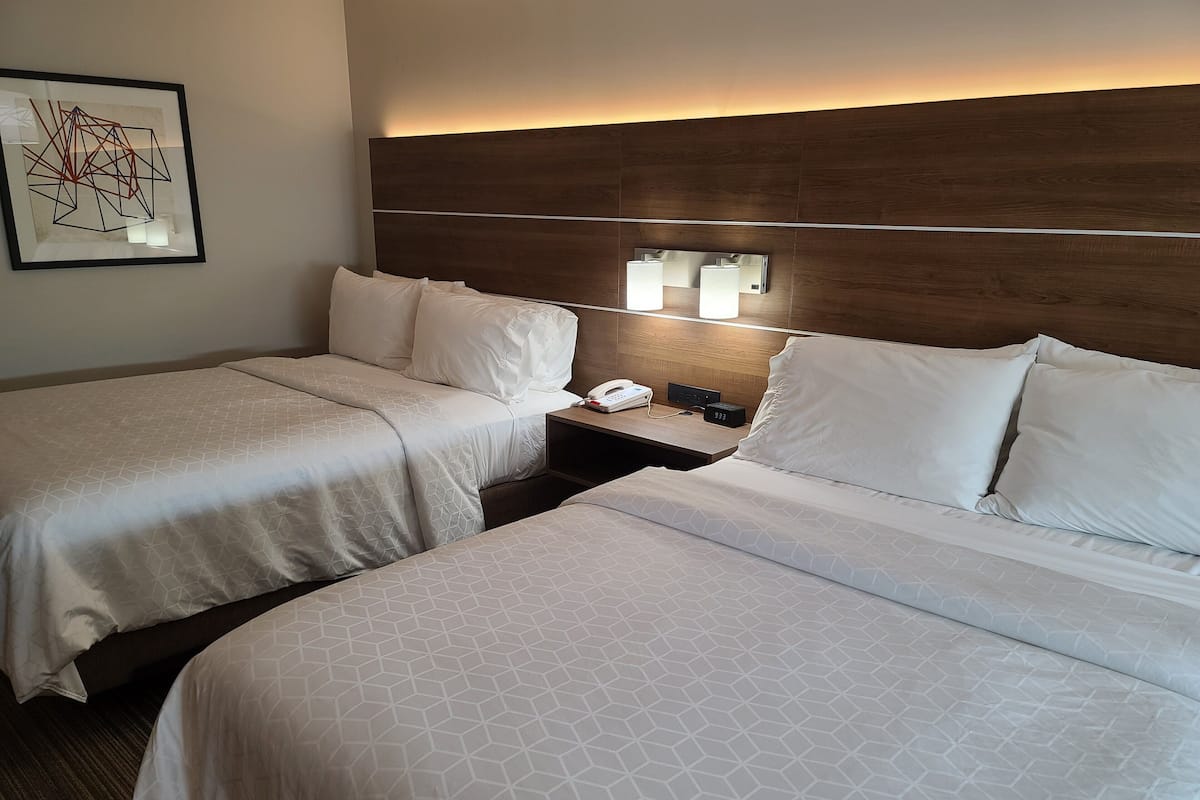 Ein Hotelzimmer mit zwei Betten, einem Nachttisch mit Telefon und Wecker sowie einem gerahmten Kunstwerk an der Wand.