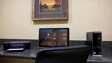 A hotel room with a desktop computer, a printer, and a framed picture on the wall.