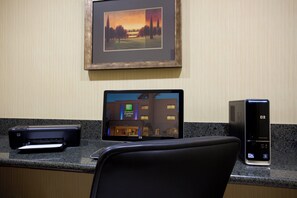 A hotel room with a desktop computer, a printer, and a framed picture on the wall.