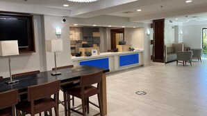 A modern hotel lobby with a reception desk, a dining area with a black table and wooden chairs, a chandelier, and a large window. - Holiday Inn Express & Suites Woodland Hills by IHG (Woodland Hills)