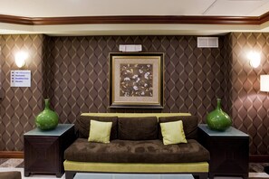 A hotel room with a brown patterned wall, a framed floral artwork, a brown sofa with cushions, two green vases, and a sign indicating guest rooms and amenities. - Holiday Inn Express & Suites Woodland Hills by IHG (Woodland Hills)