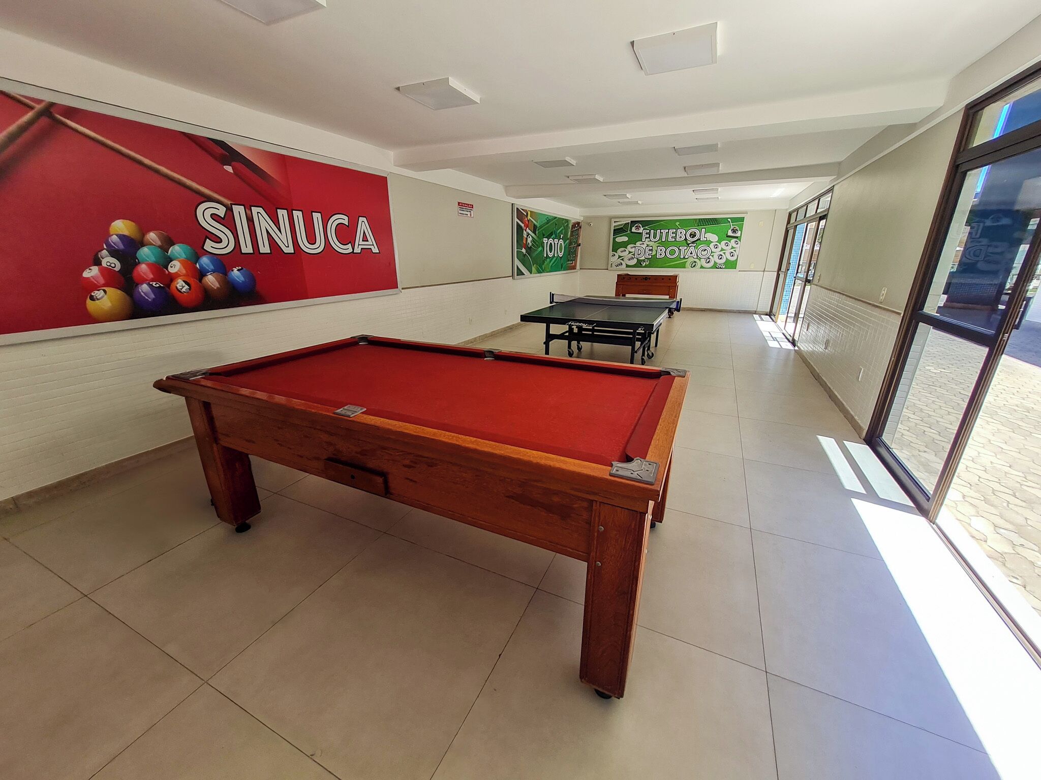 A billiards room with a pool table, a red wall with billiard balls, and a green wall with a 'FUTEBOL DE BOTAO' sign.