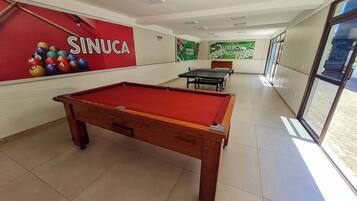 A billiards room with a pool table, a red wall with billiard balls, and a green wall with a 'FUTEBOL DE BOTAO' sign.