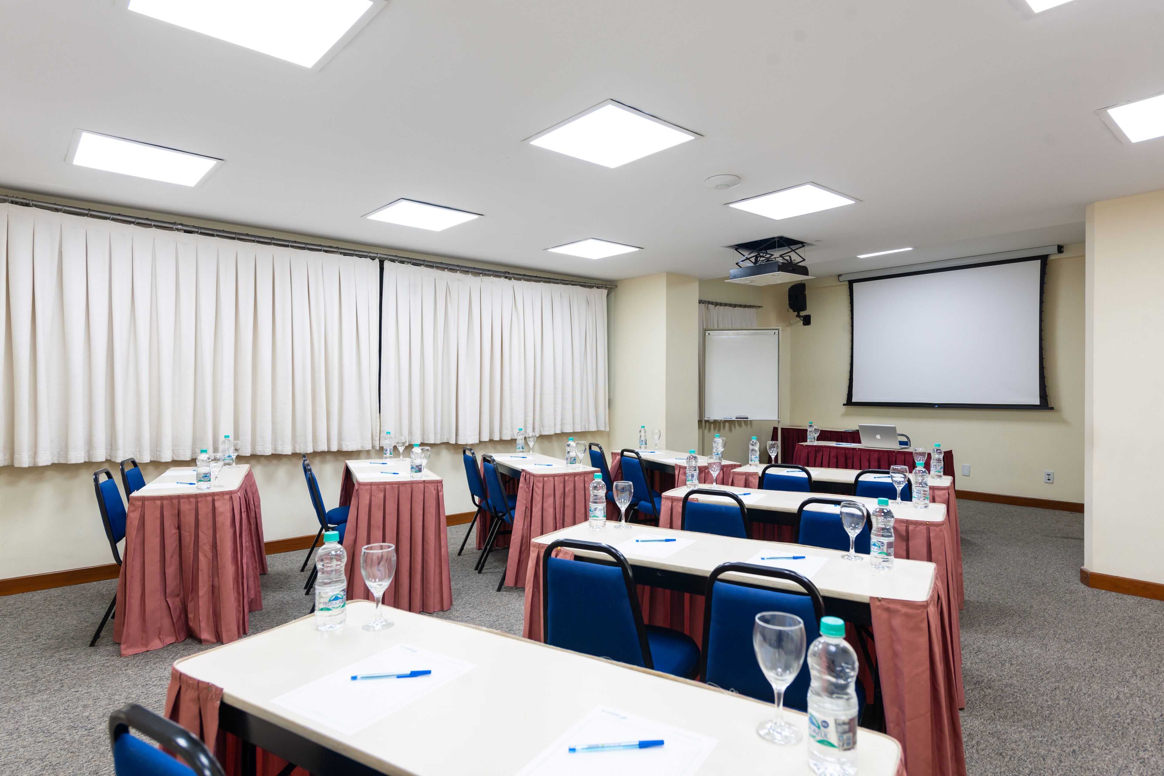 Uma sala de conferências com mesas, cadeiras e uma tela de projetor.