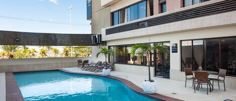 A modern hotel with a swimming pool, outdoor seating, and a view of palm trees.
