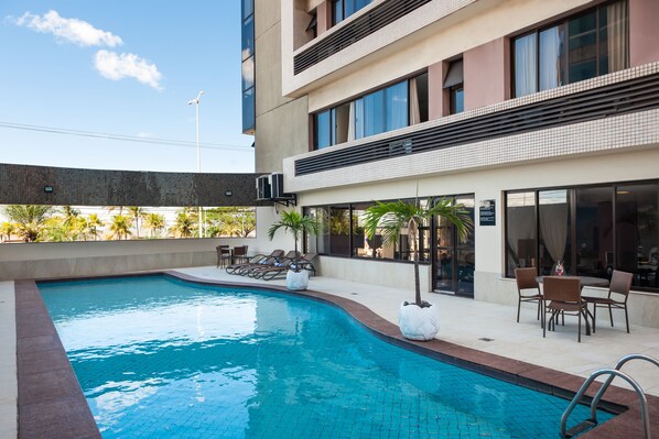 A modern hotel with a swimming pool, outdoor seating, and a view of palm trees. - Slaviero Vitória (Vitoria)