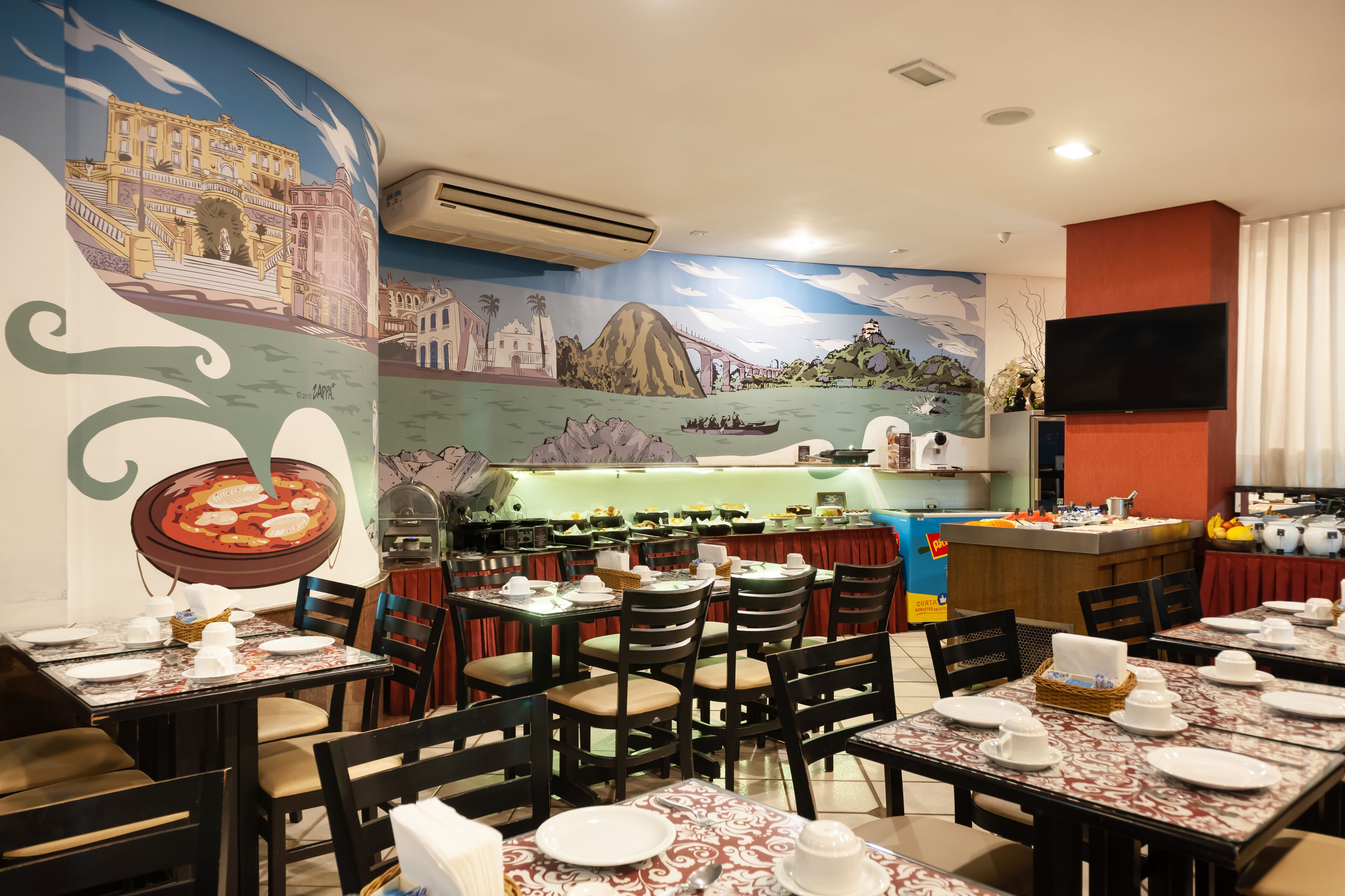 Un ristorante con diversi tavoli apparecchiati per consumare i pasti, un'area cucina e un murale raffigurante un paesaggio urbano e una distesa d'acqua.