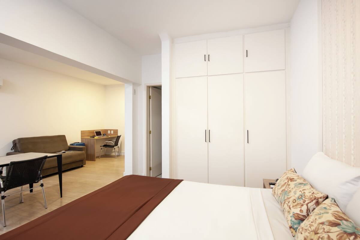 Ein Hotelzimmer mit Bett, Schreibtisch mit Laptop, Sofa und Kleiderschrank.