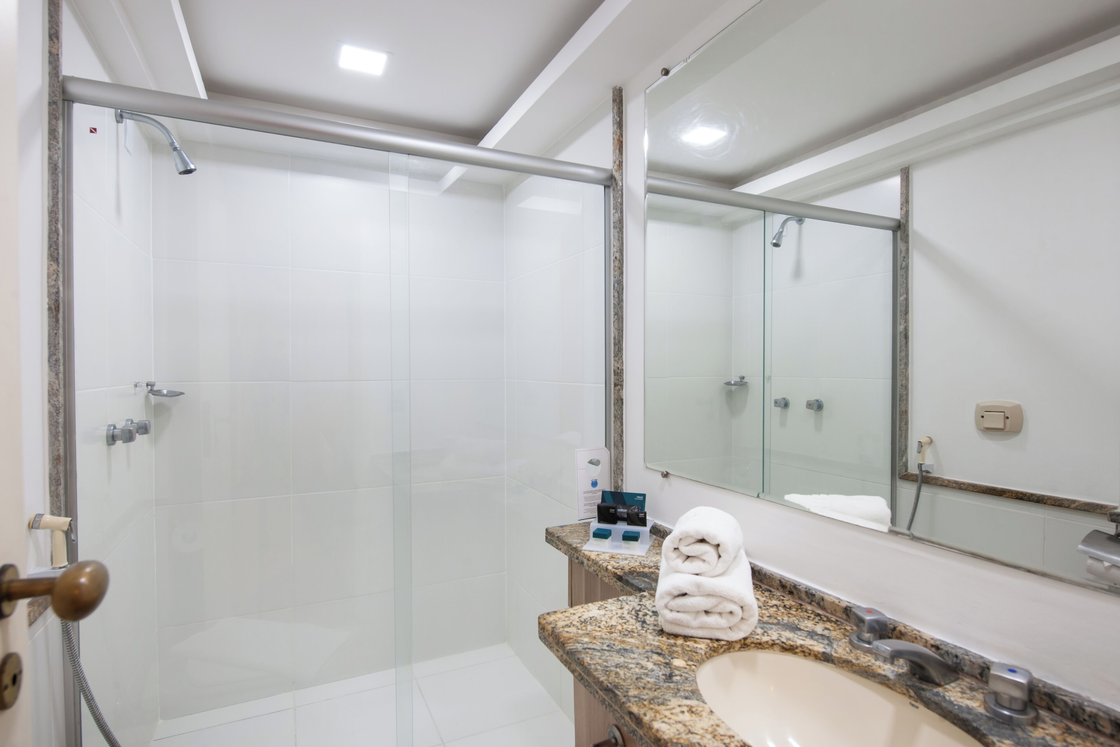 A modern bathroom with a glass-enclosed shower, a granite countertop, and a large mirror.