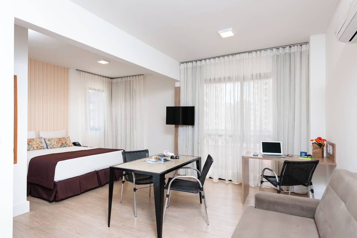 Ein modernes Hotelzimmer mit Bett, Schreibtisch mit Laptop, Fernseher und einer Couch.