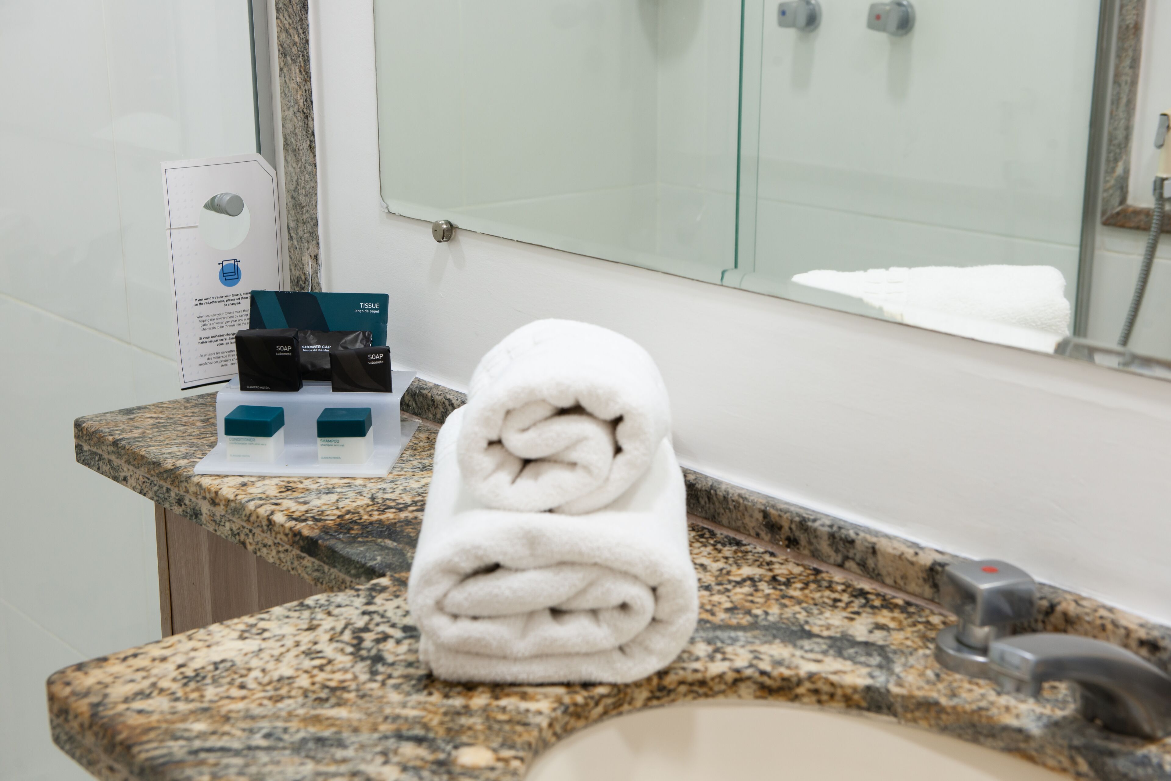 A bathroom with a granite countertop, a white towel, and soap dispensers.