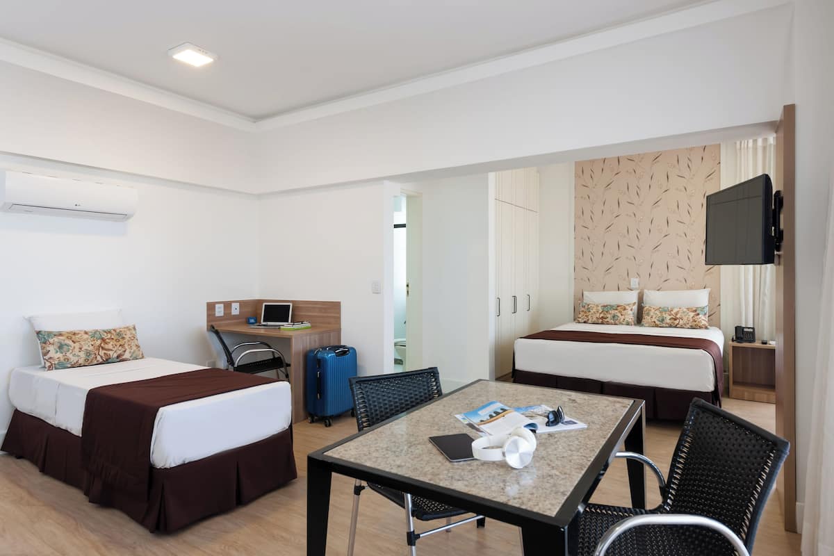 Ein Hotelzimmer mit zwei Betten, einem Schreibtisch, einem Fernseher und einem Tisch mit Stühlen.
