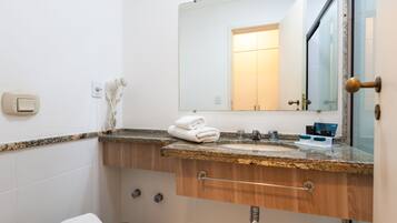 A bathroom with a granite countertop sink, a towel rack with folded towels, a mirror, and a door with a brass handle.