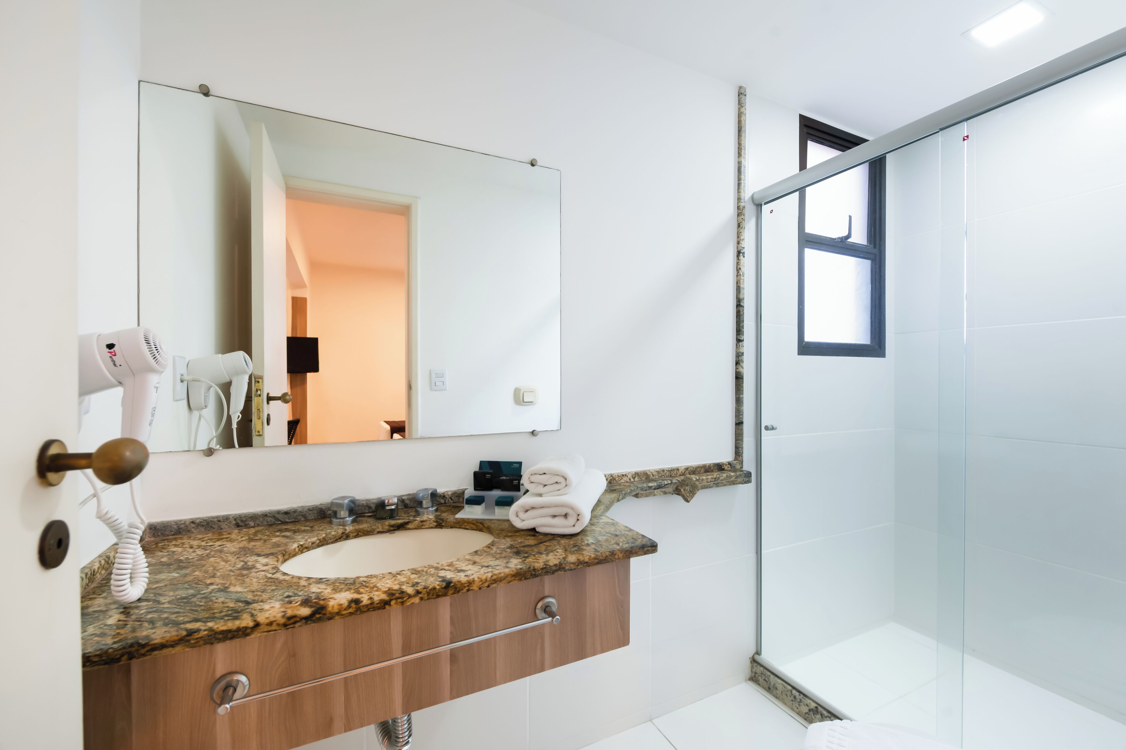 Un baño con encimera de granito, tocador de madera, espejo grande y cabina de ducha de vidrio.