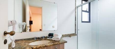 Un baño con encimera de granito, tocador de madera, espejo grande y cabina de ducha de vidrio.
