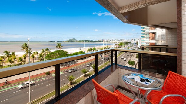 Een balkon met uitzicht op een strand en stadsbeeld, met een tafel, stoelen en een tijdschrift.