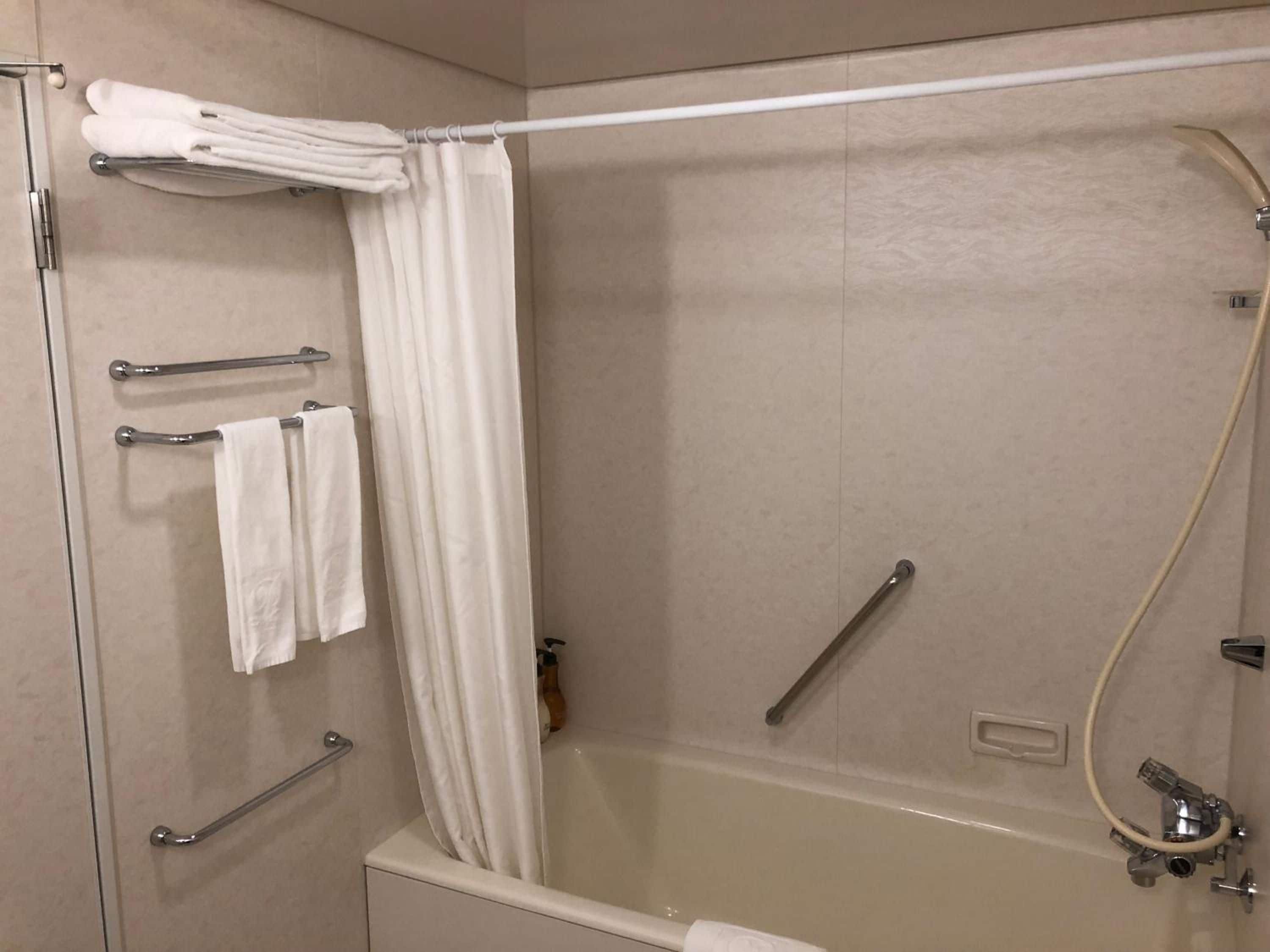 A modern bathroom with a bathtub, a shower area, and a toilet. There are grab bars installed for safety, and a towel rack with towels.