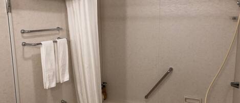 Un baño moderno con bañera, zona de ducha y retrete. Cuenta con barras de apoyo para seguridad, y un perchero con toallas.