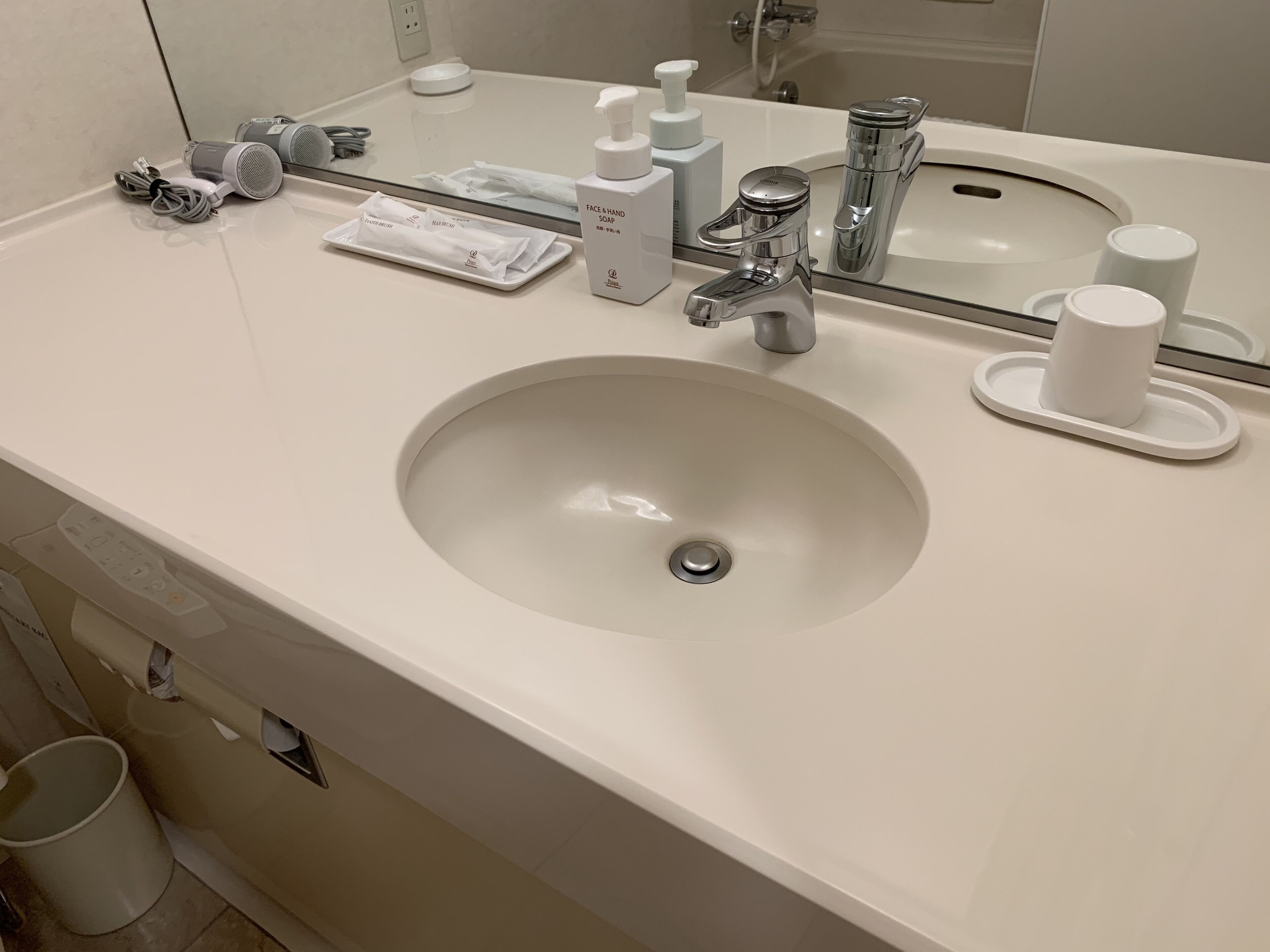 A bathroom with a white sink, a mirror, a faucet, and a cup holder.