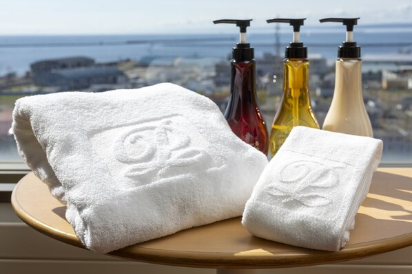 A bathroom with a window view of a cityscape, a wooden stool, and three bottles of toiletries. - Kushiro Prince Hotel (Kushiro)