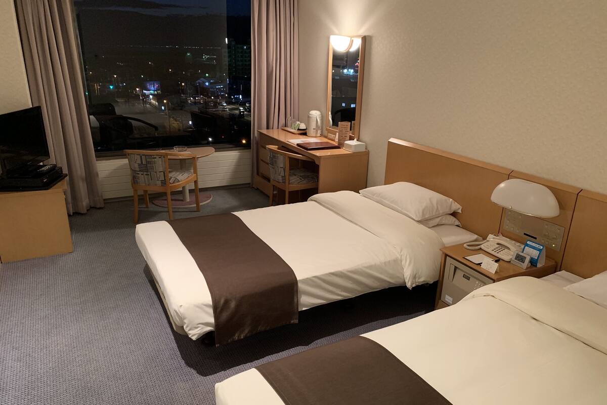A hotel room with two beds, a desk, a chair, a TV, and a city view.
