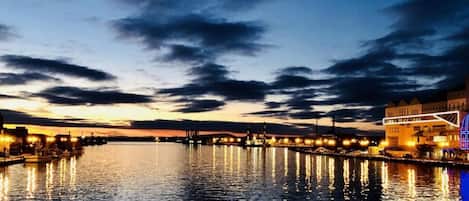 Vista al agua al atardecer con edificios iluminados y un río tranquilo que refleja las luces.