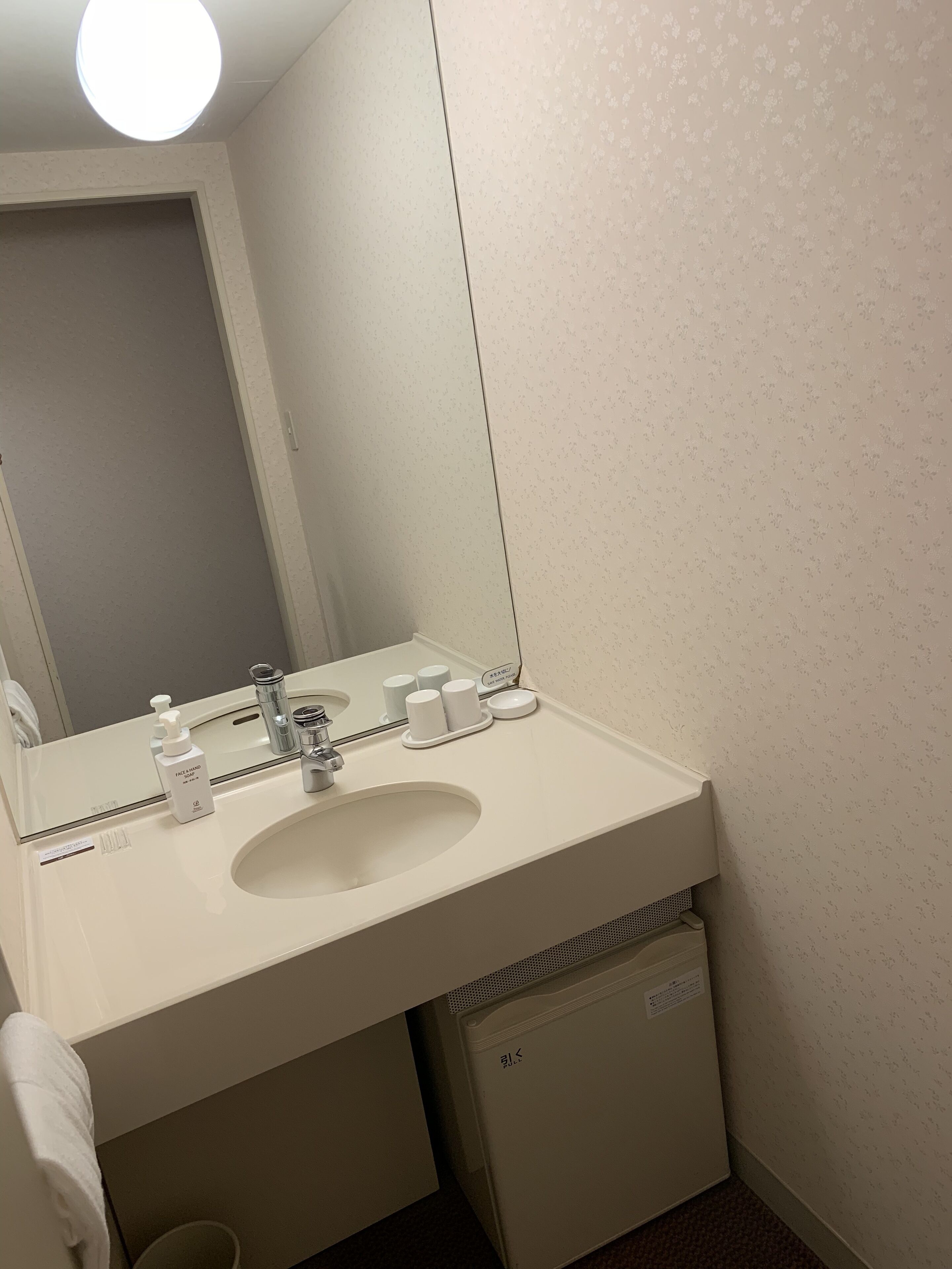 A bathroom with a white sink, a mirror, a towel, and a trash bin.