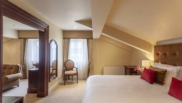 A hotel room with a large bed, a sitting area with a sofa, a chair, a mirror, and a nightstand with a lamp.