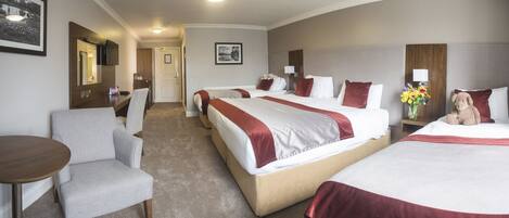 A hotel room with two beds, a sitting area with a chair, a small table, and a desk.