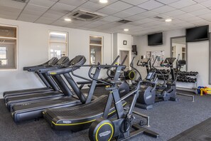 A gym with multiple treadmills, elliptical machines, and a wall-mounted TV.