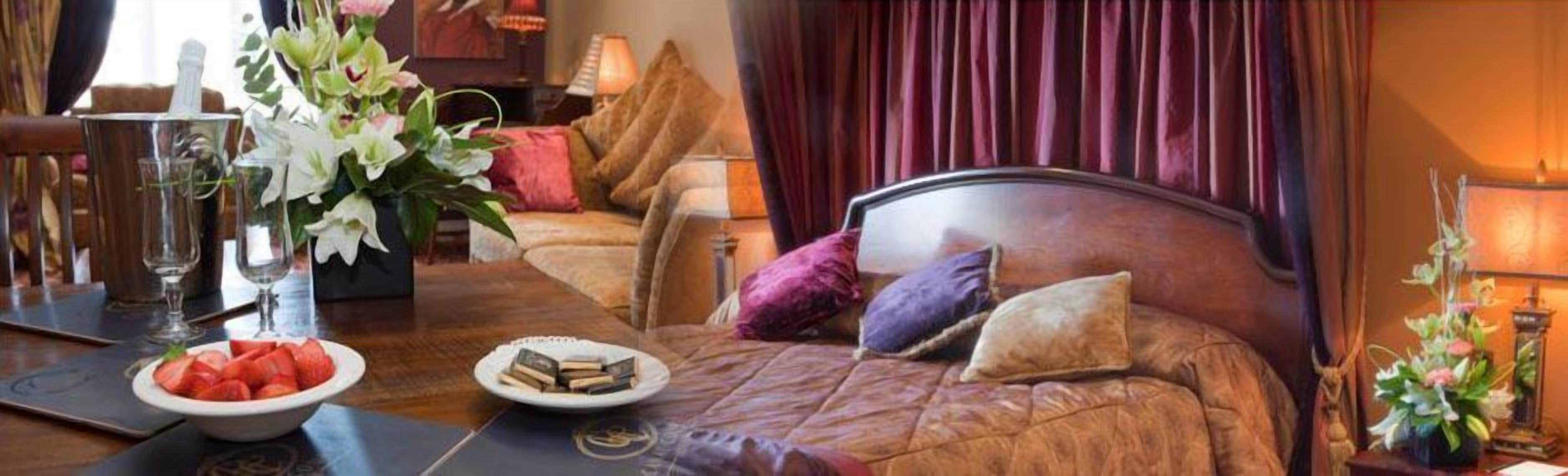 A well-appointed bedroom with a large bed, a bedside table, a vase with flowers, and a bowl of strawberries.