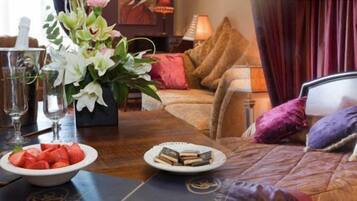 A well-appointed bedroom with a large bed, a bedside table, a vase with flowers, and a bowl of strawberries.