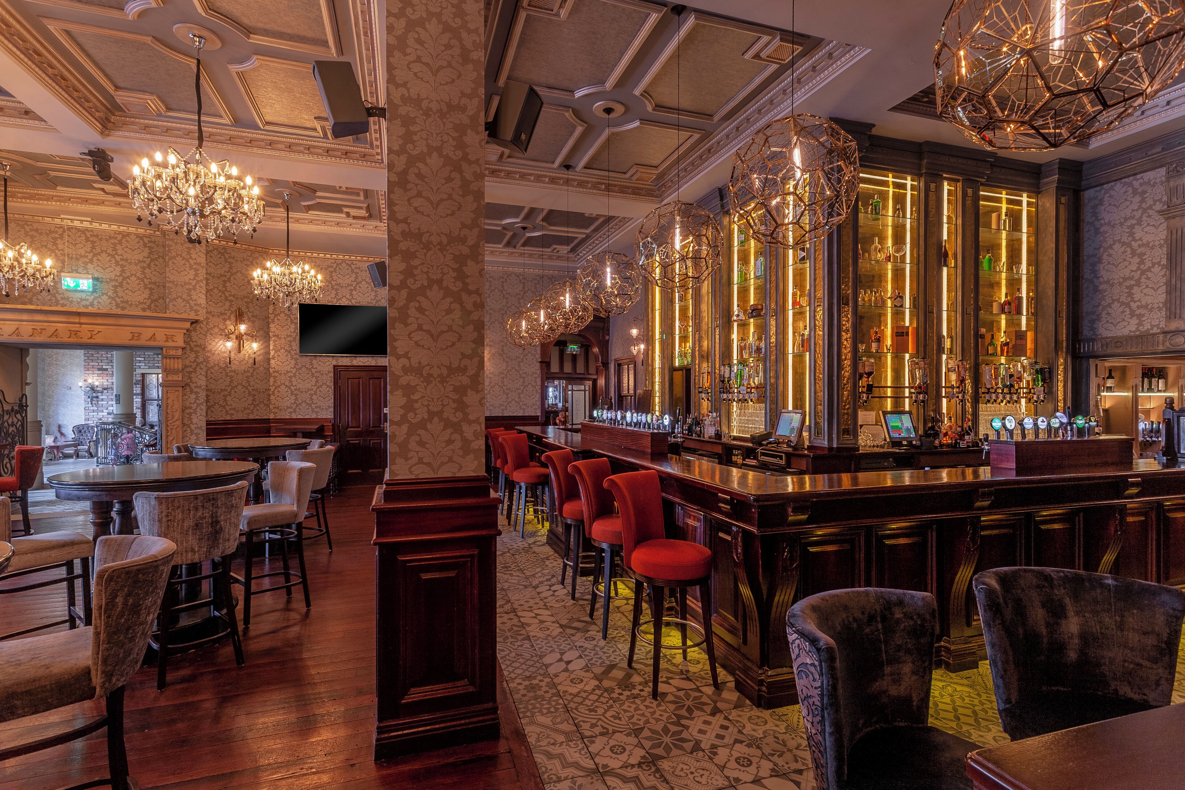A bar area with a long counter, multiple bar stools, and a television screen.