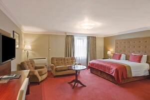 Una habitación de hotel con cama, sofá, mesa, televisión y ventana con cortinas.