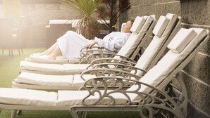 A row of sun loungers with white cushions, arranged in an outdoor patio area with a stone wall backdrop and a green artificial turf floor. - Canal Court Hotel (Newry)