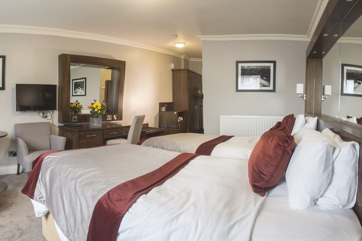 A hotel room with two beds, a sitting area with a chair and a small table, a dresser, and a large mirror.