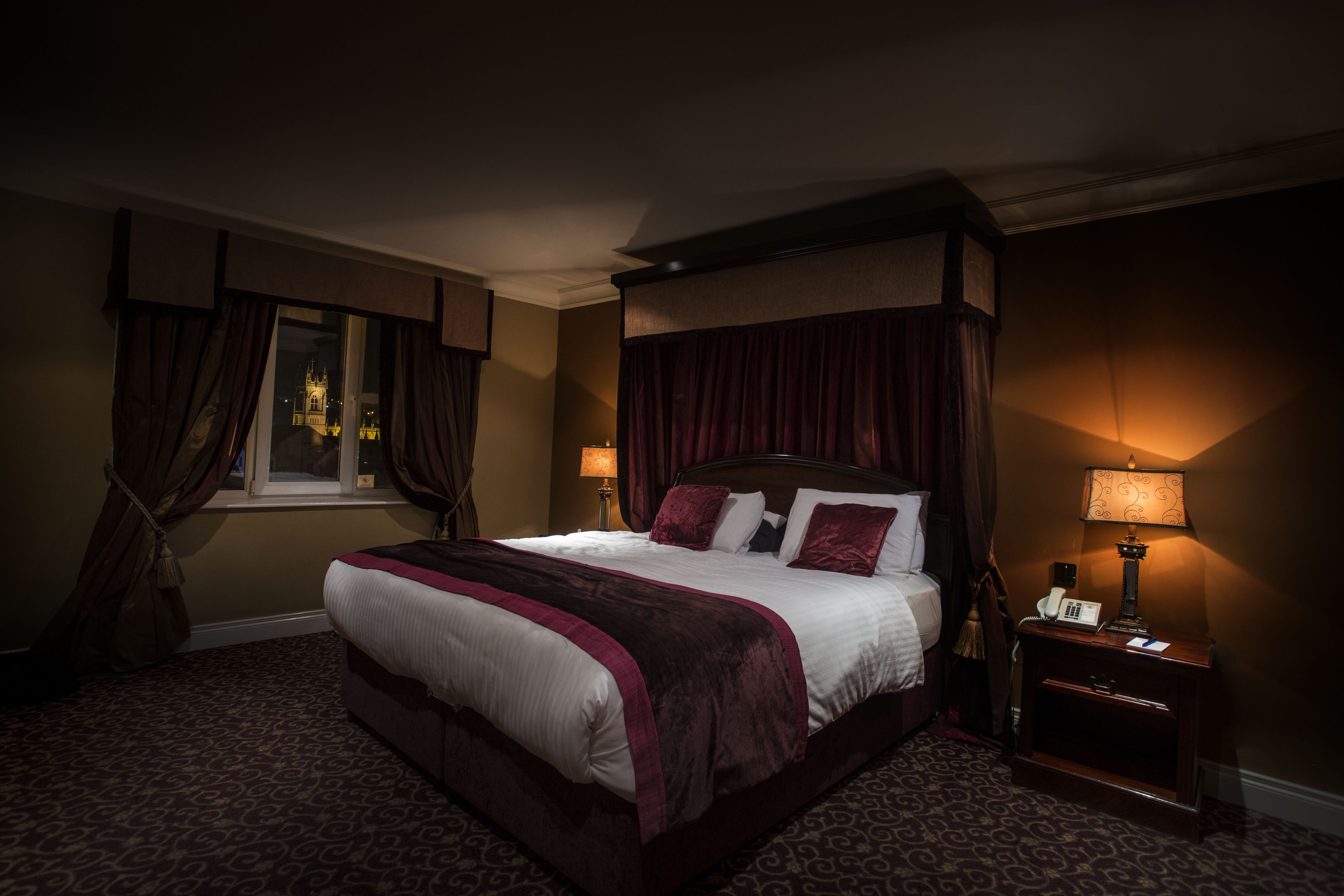 A hotel room with a large bed, a nightstand with a lamp, and a window with curtains.