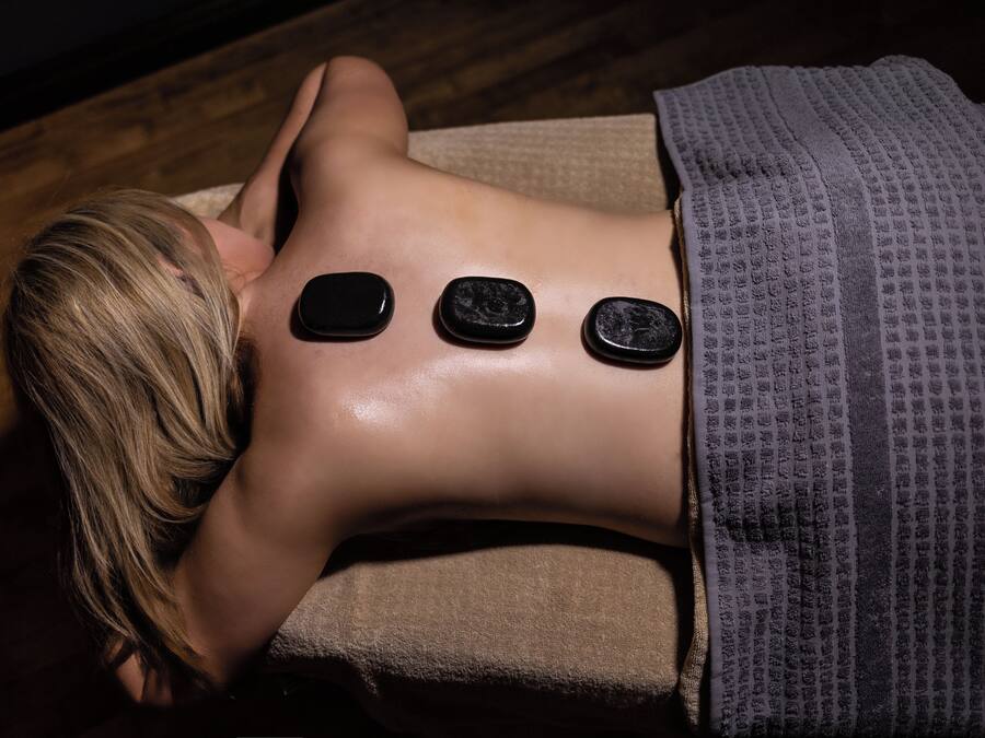 A person lying on a massage table with three stones placed on their back.