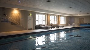 An indoor swimming pool with tiled walls, a tiled floor, and a sunlit room with windows and lounge chairs. - Canal Court Hotel (Newry)